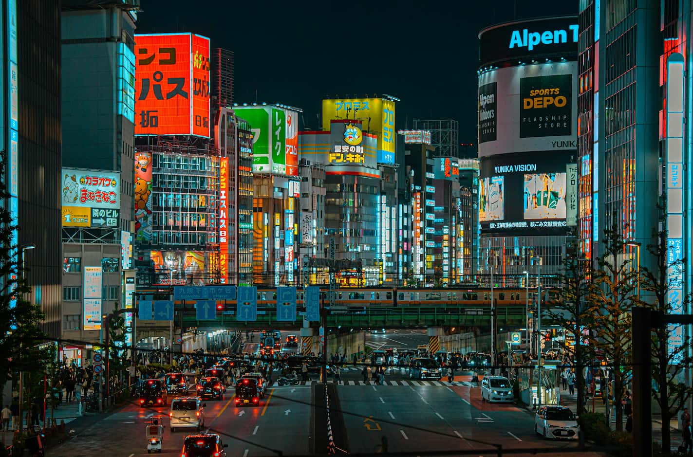 Shibuya district in Tokyo at night with bright neon billboards, city traffic, and an elevated train passing between illuminated buildings.